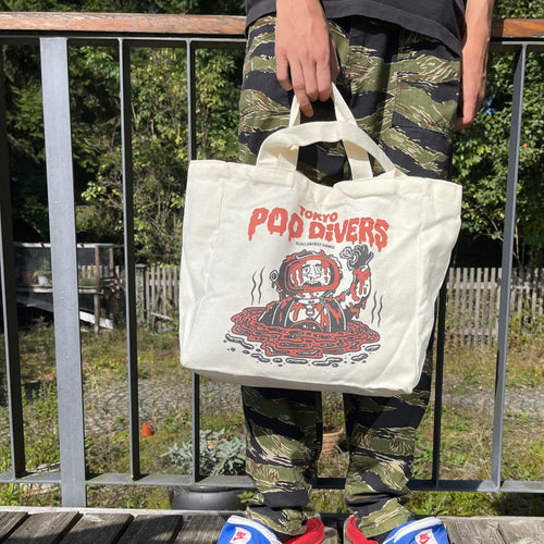 „Tokyo Poo Divers“ Tote Bag von Heldbergs Games, aus 16-Unzen-Baumwolle. Maße 32 x 33 x 16 cm, mit Magnetverschluss und Innentasche. Freches Design für urbane Legenden.