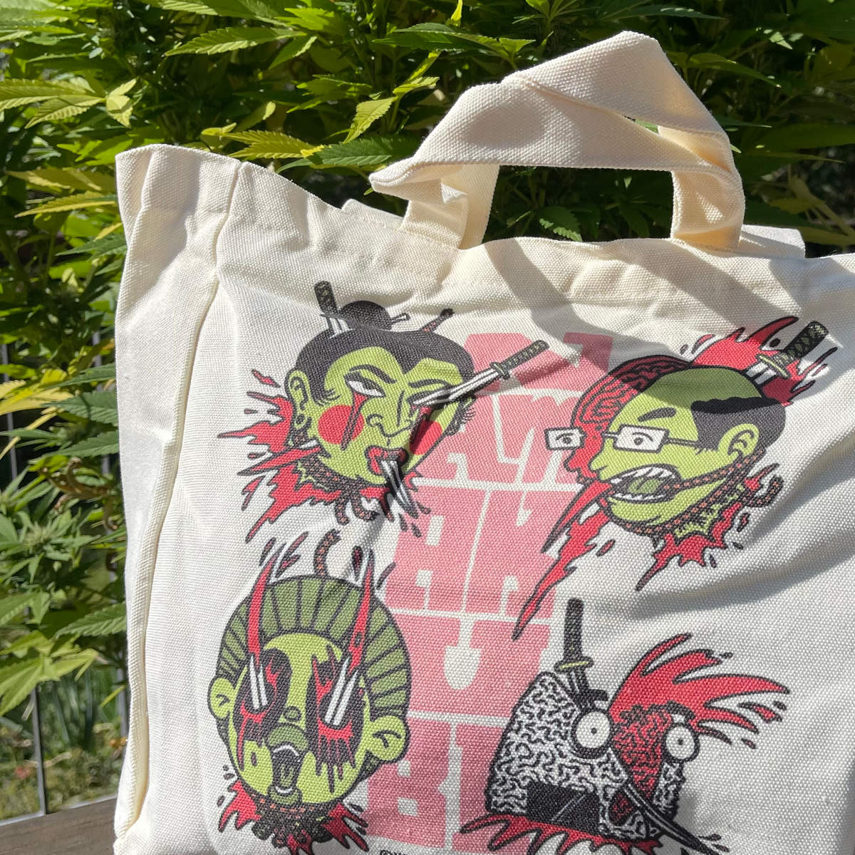 „Namakubi“ Tote Bag von Heldbergs Games mit vier ikonischen Köpfen, aus 16-Unzen-Baumwolle. Maße 32 x 33 x 16 cm, mit Magnetverschluss und Innentasche. Japanisches Design trifft auf praktischen Stil.